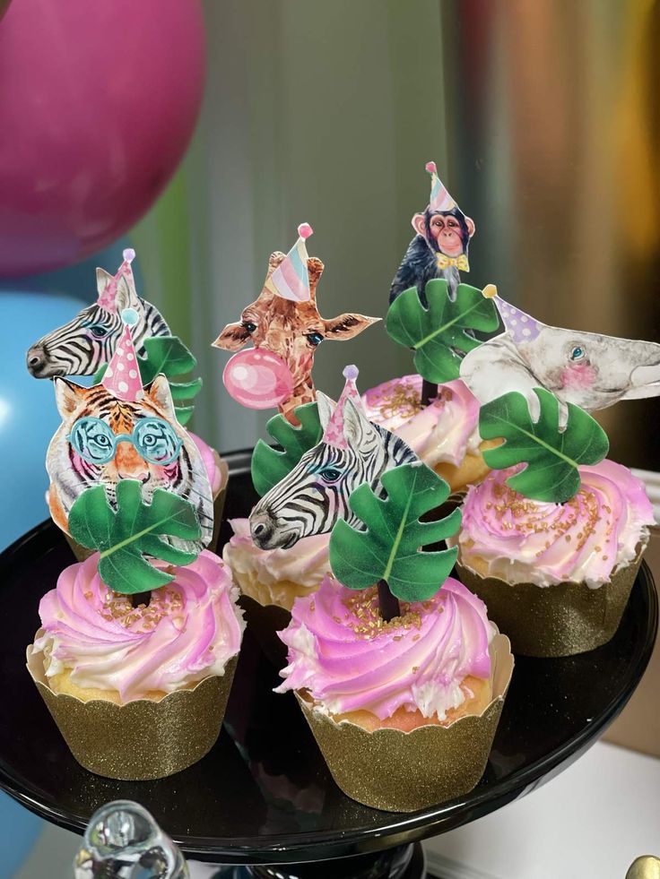 cupcakes with pink frosting and zebra decorations on a black cake platter