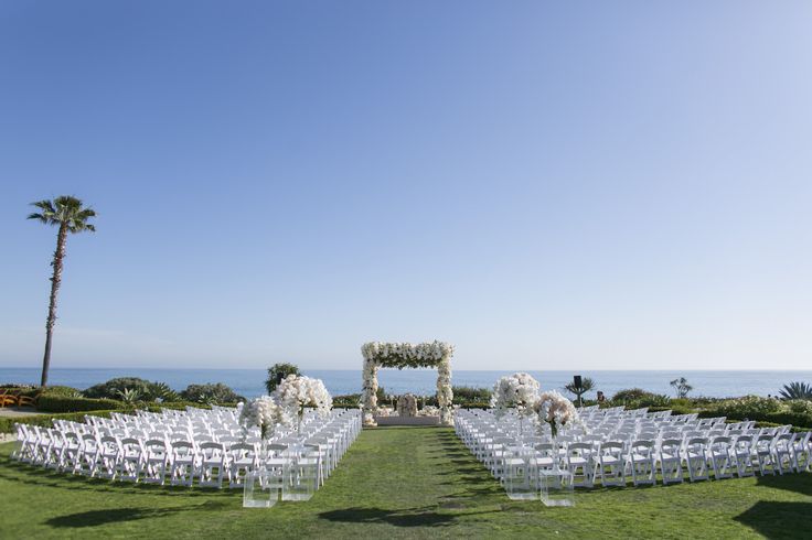 an outdoor ceremony set up with white flowers and greenery on the lawn next to the ocean