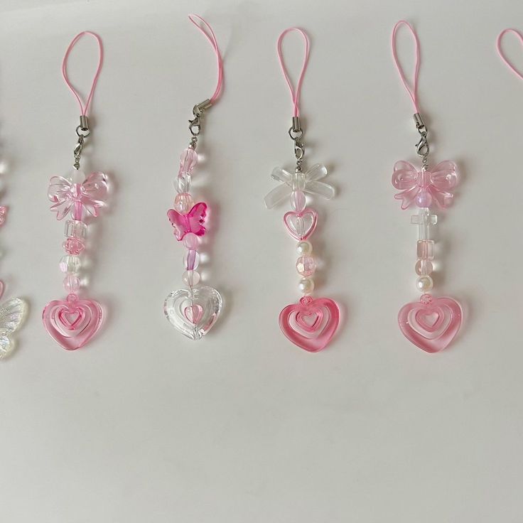 five different necklaces with hearts and bows hanging from hooks on a white surface,