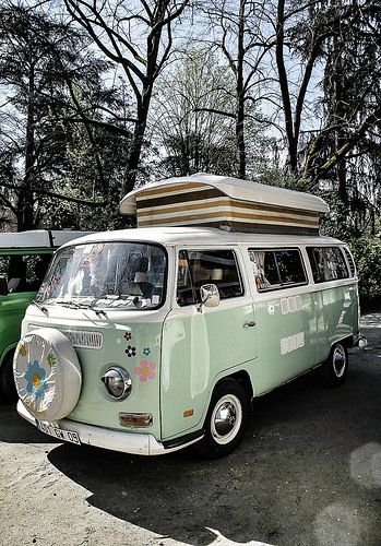 an old vw bus is parked in front of another van with a camper on top