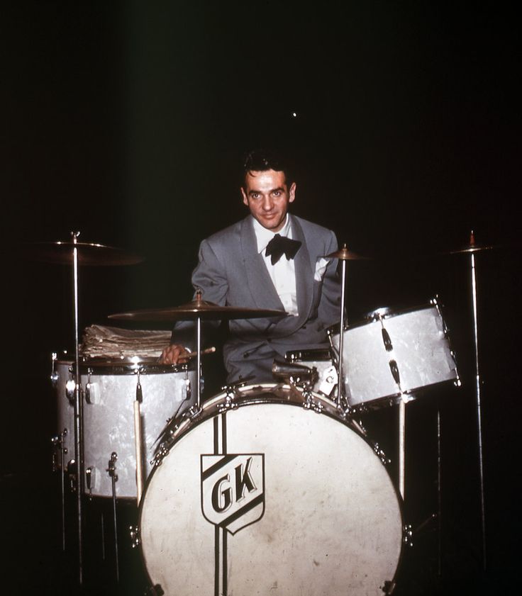 a man in a suit and bow tie sitting behind a drum set with cyl drums