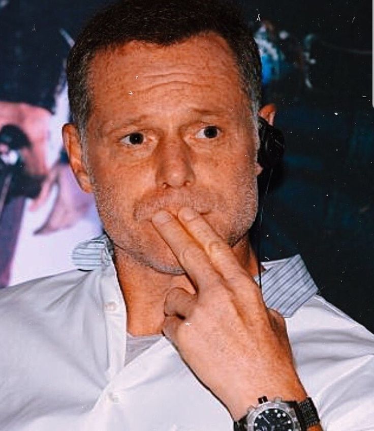 a man with his hand to his mouth in front of a movie poster and looking at the camera