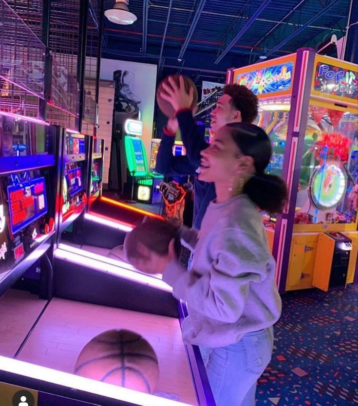 two people are playing video games in a pinball game room with arcade machines and basketball hoops