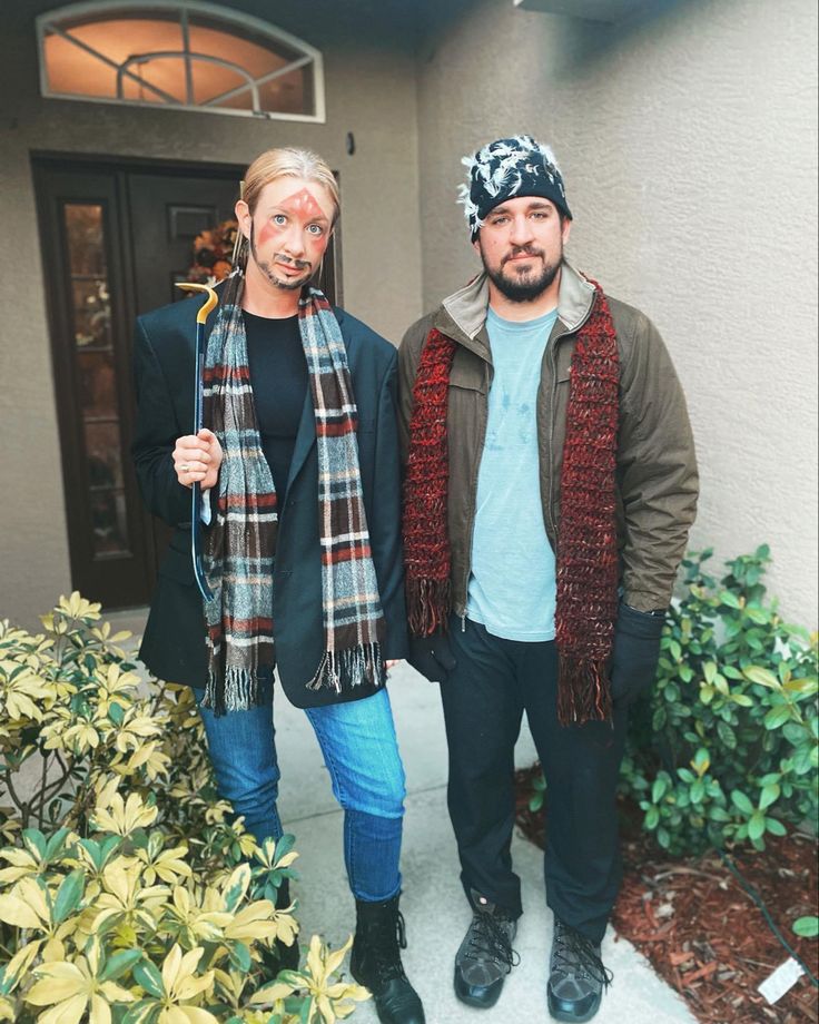 two men standing next to each other in front of a house wearing scarves and scarfs