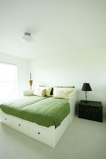 a bed with green sheets and pillows in a white room next to a black dresser