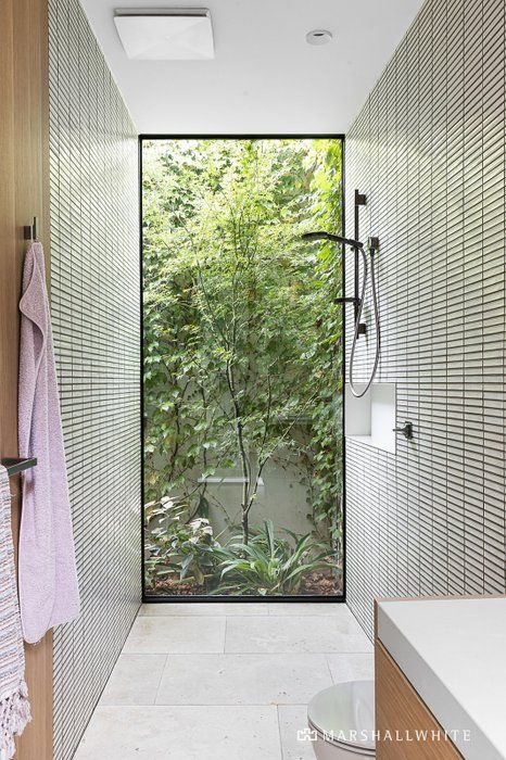 a bathroom with a glass door leading into the shower area and outside trees in the background