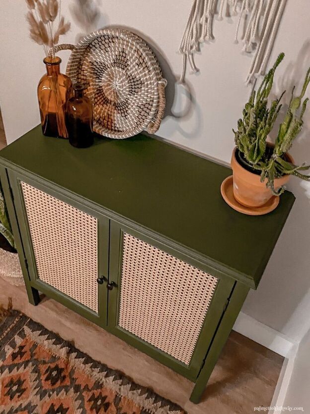 a green cabinet with wicker doors next to a potted plant and other decorative items