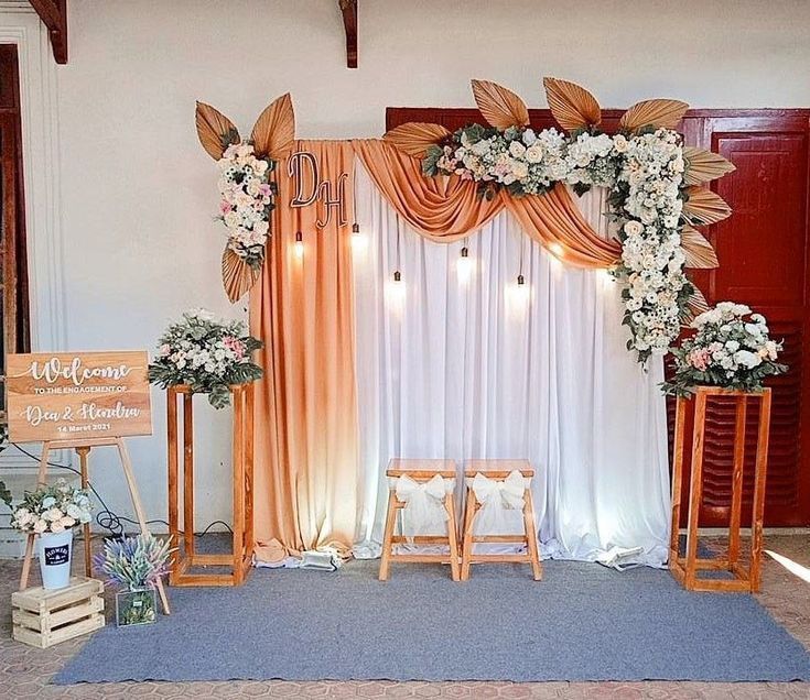 a decorated stage with white flowers and greenery on the side, surrounded by orange drapes