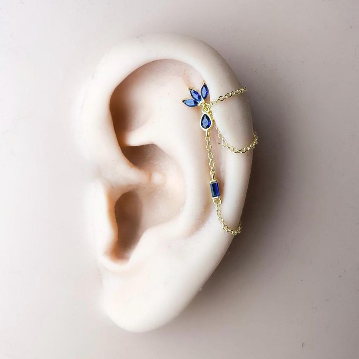 an ear with a chain attached to it and some blue beads hanging from the side