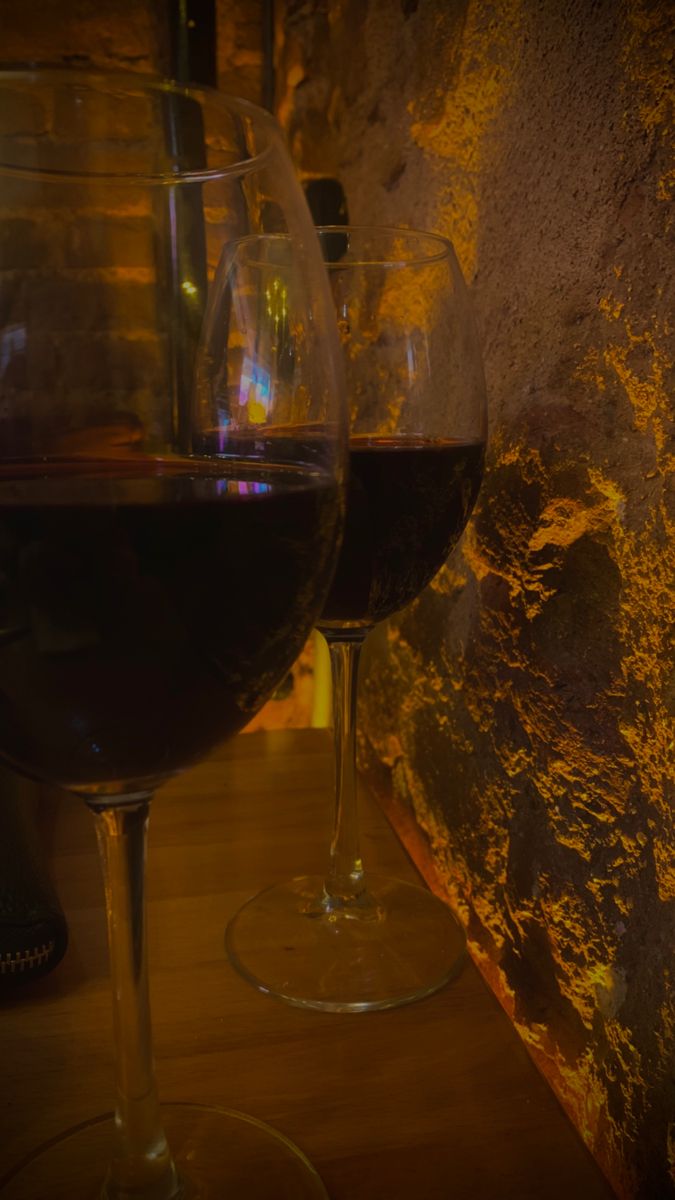 two glasses of wine sitting next to each other on a wooden table in front of a stone wall