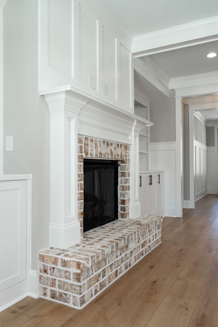 an empty living room with a brick fireplace and white painted walls, hardwood flooring