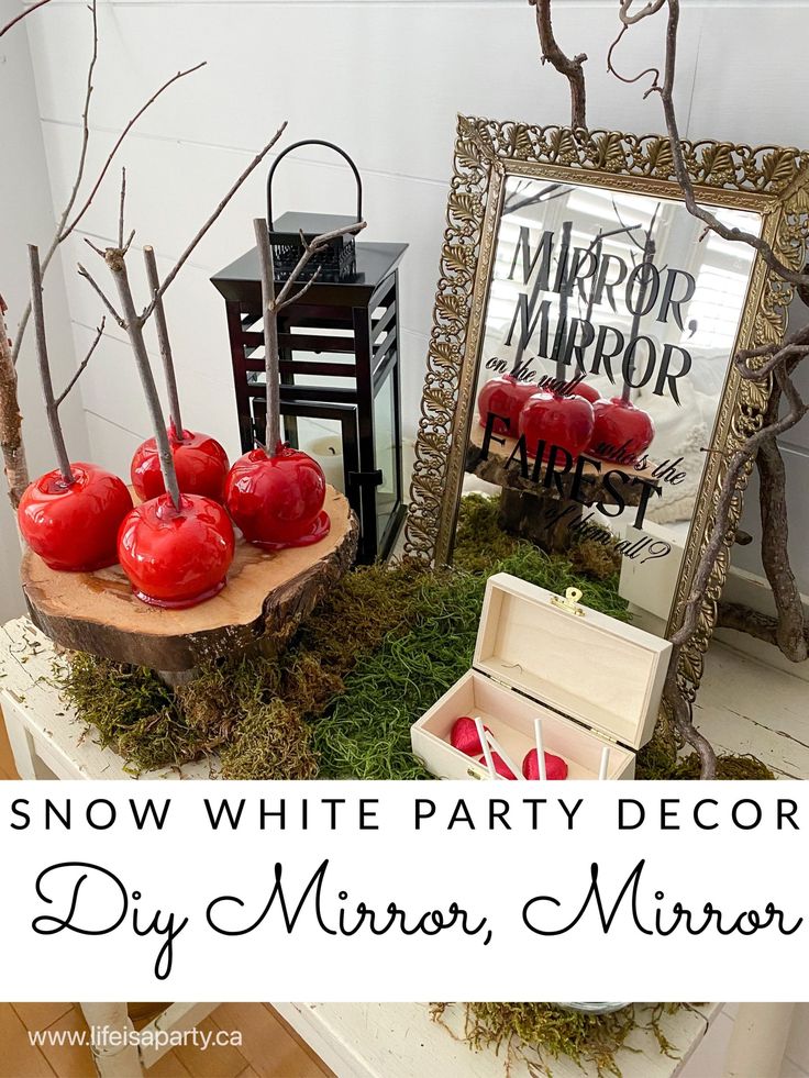 snow white party decor with red apples and moss in front of a mirror on a table