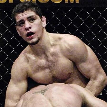 a man with no shirt standing in front of a chain link fence and posing for the camera