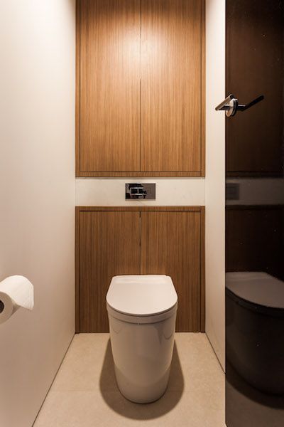 a toilet in a bathroom next to a roll of toilet paper and wooden cabinet doors