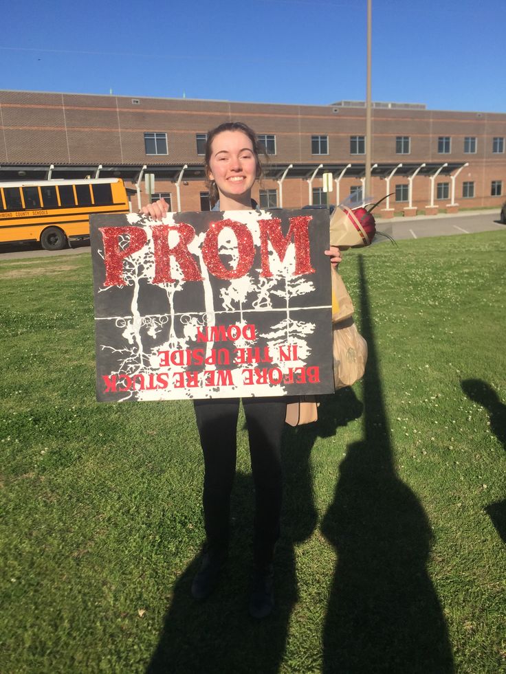 a woman holding up a sign in front of a school building with the word prom written on it