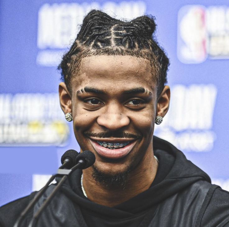 a man with dreadlocks smiles while speaking into a microphone