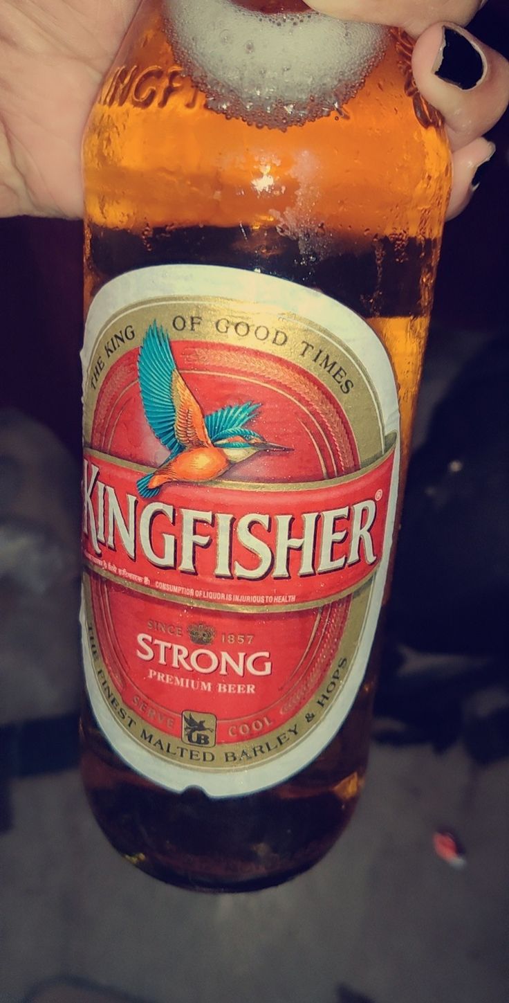 a person holding up a beer bottle with the word kingfisher written on it