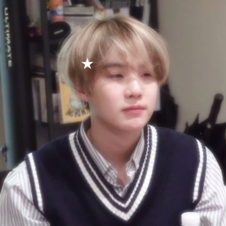 a young man with blonde hair wearing a sweater vest and looking at the camera while sitting down