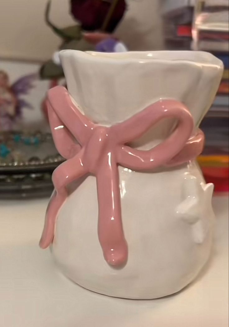 a white vase with a pink bow on the front and bottom, sitting on a table