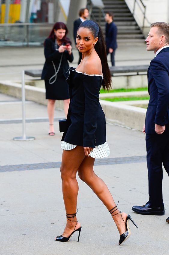 a woman in black and white dress walking down the street with two men behind her