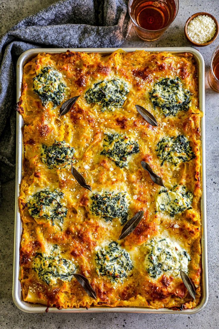 a casserole with spinach and cheese in a pan next to two glasses