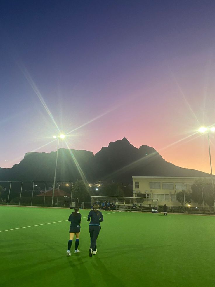 two soccer players are walking on the field at night, with mountains in the background