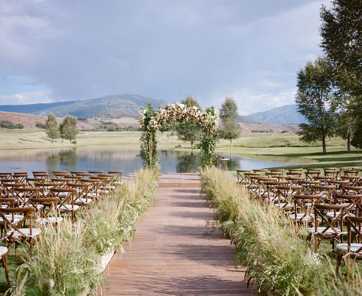 an outdoor wedding ceremony setup with chairs and flowers on the aisle, overlooking a lake