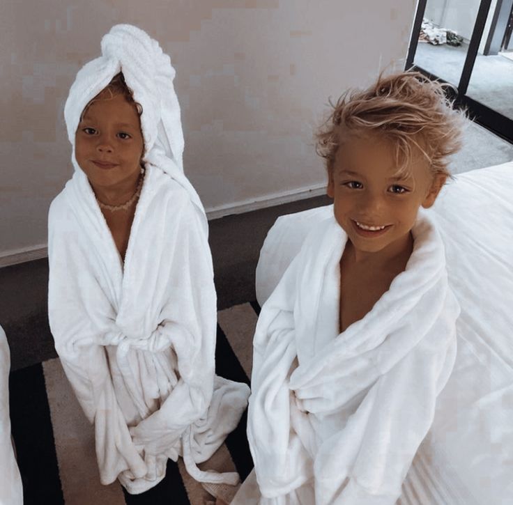 two children wrapped in white towels sitting on a bed