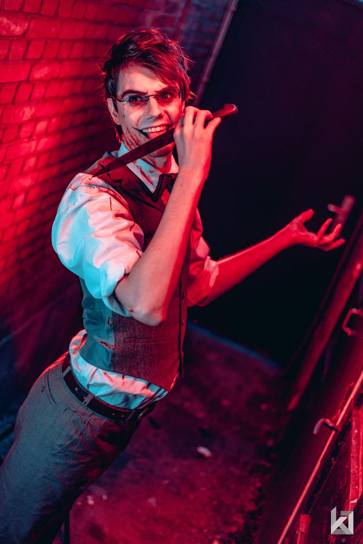 a man with painted face and tie standing in front of a brick wall