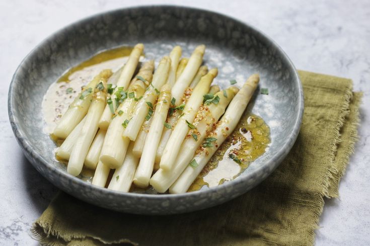 a bowl filled with white asparagus on top of a green cloth next to a napkin