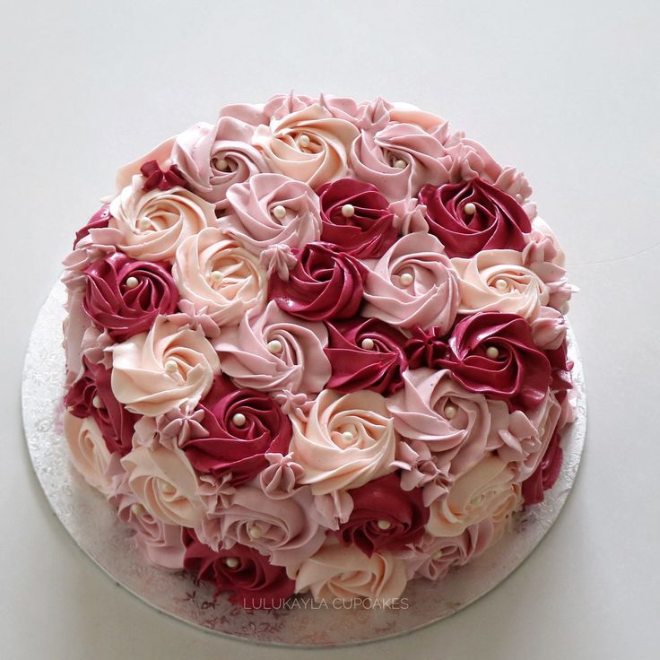 a cake with pink and red frosting flowers on it sitting on a white table