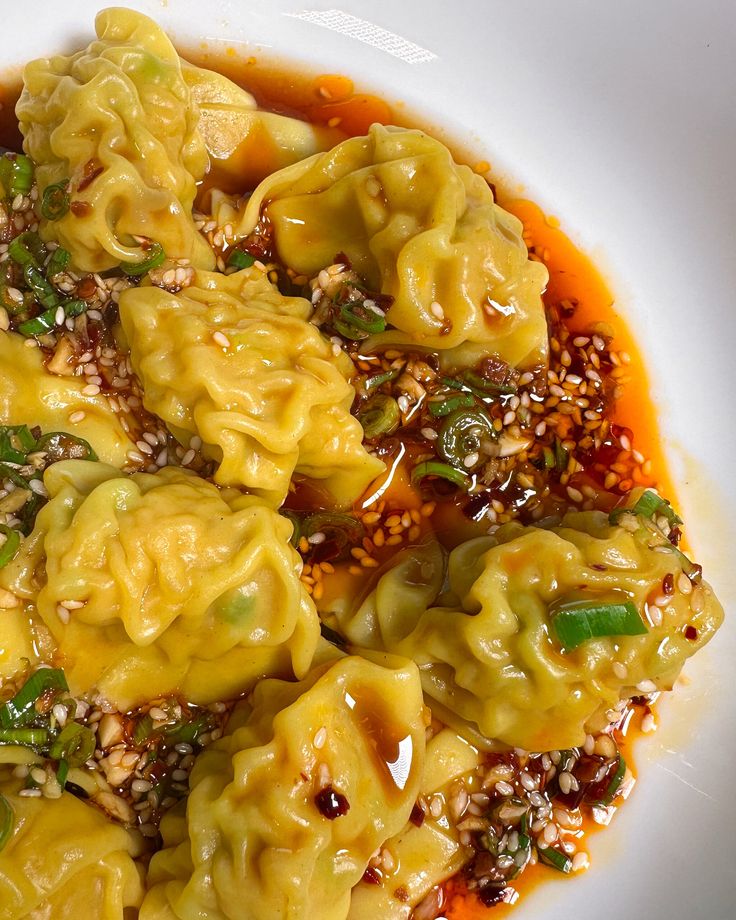 a white plate topped with dumplings covered in sauce and green peppers on top of sesame seeds