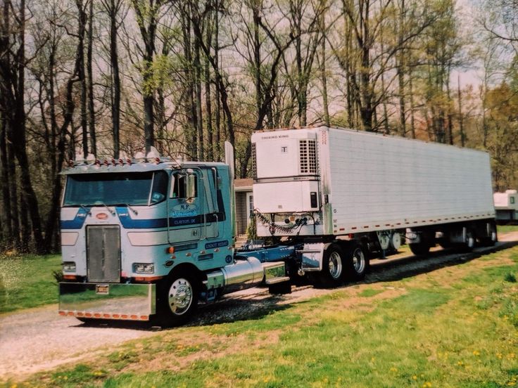 a semi truck hauling a trailer down a road in front of some trees and grass