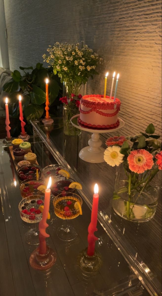 a table topped with cakes and candles next to vases filled with flowers on top of it