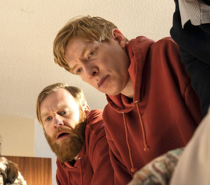 two men in red hoodies are looking at the camera with one man's face partially obscured by his hands