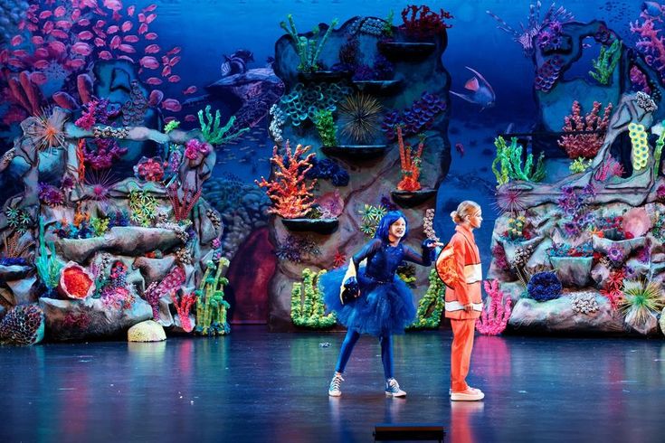 two people are performing on stage in front of an underwater scene with corals and fish