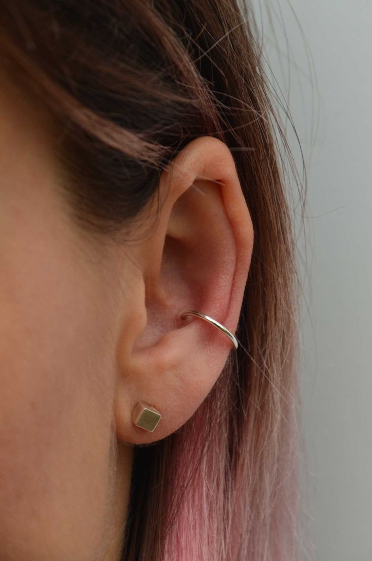 a close up of a person wearing a pair of ear piercings with pink hair