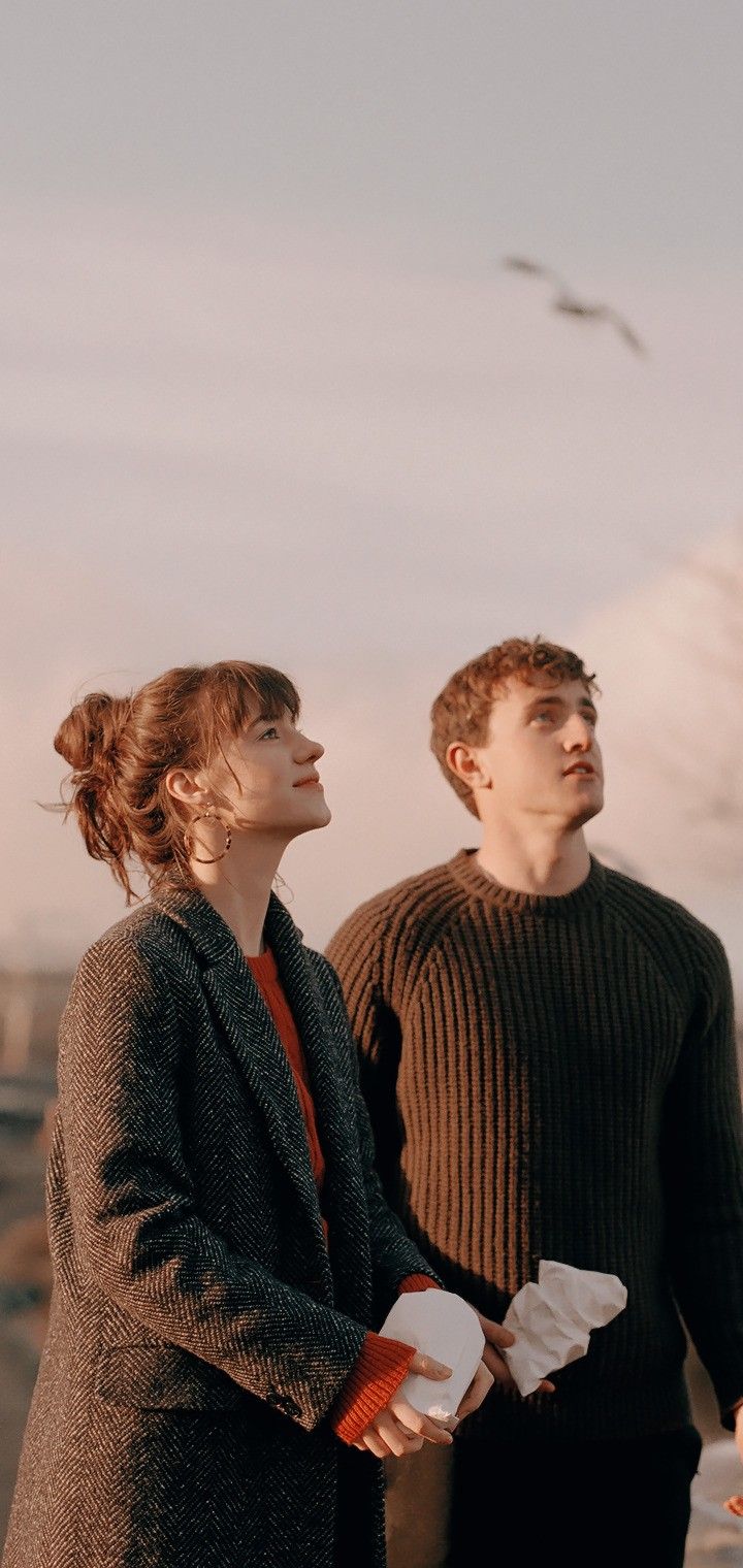 two people standing next to each other with birds flying in the sky behind them on a cloudy day