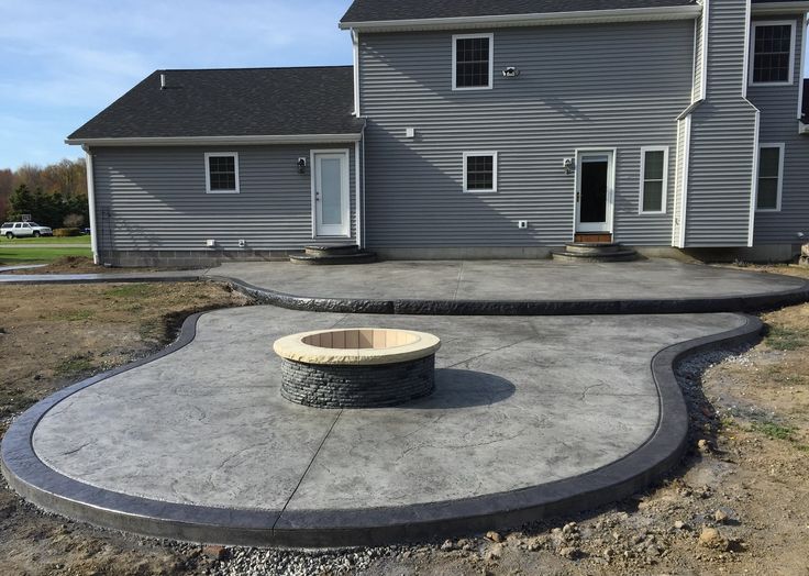 a concrete patio in front of a house with a fire pit on the ground next to it