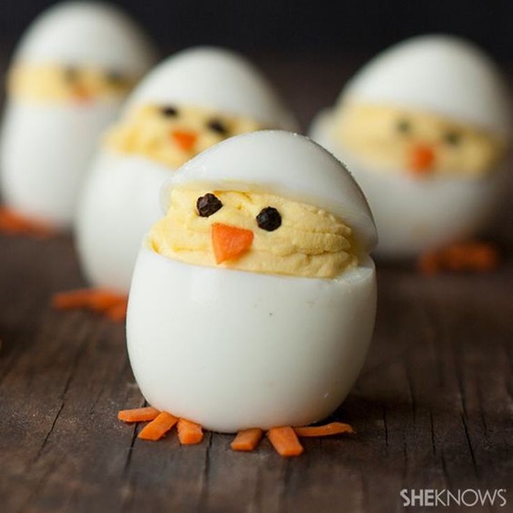 eggs with faces made to look like chickens sitting in an egg shell on a wooden table