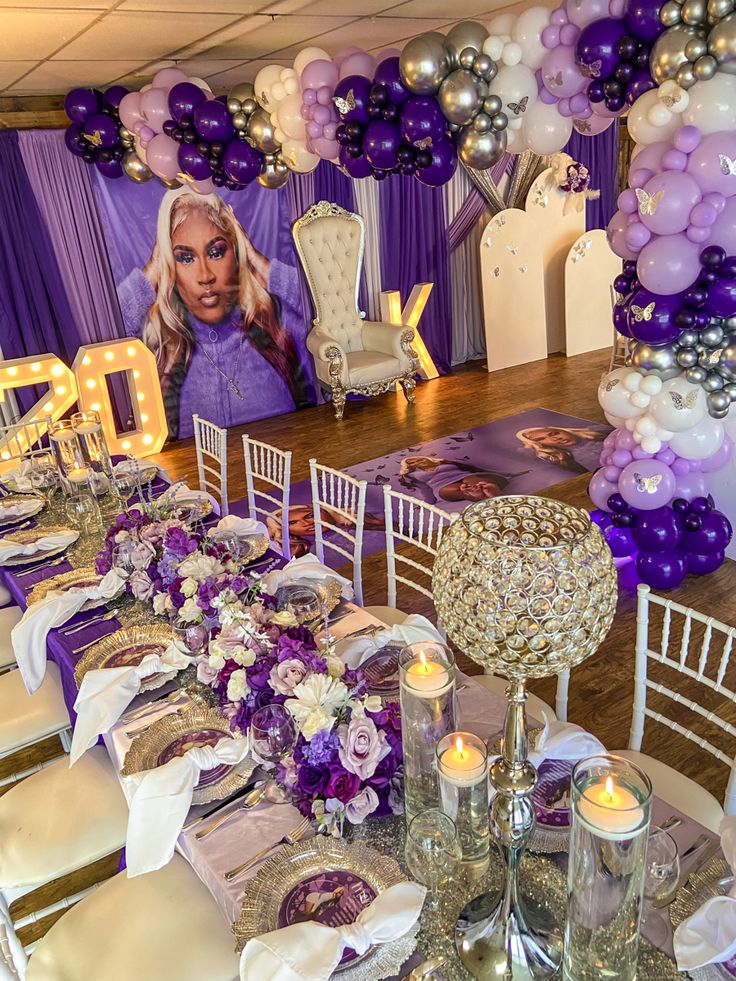 the table is set with purple and white balloons, silver chairs, and candles on it