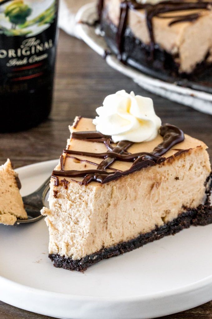 a piece of cheesecake on a white plate with chocolate drizzle and whipped cream