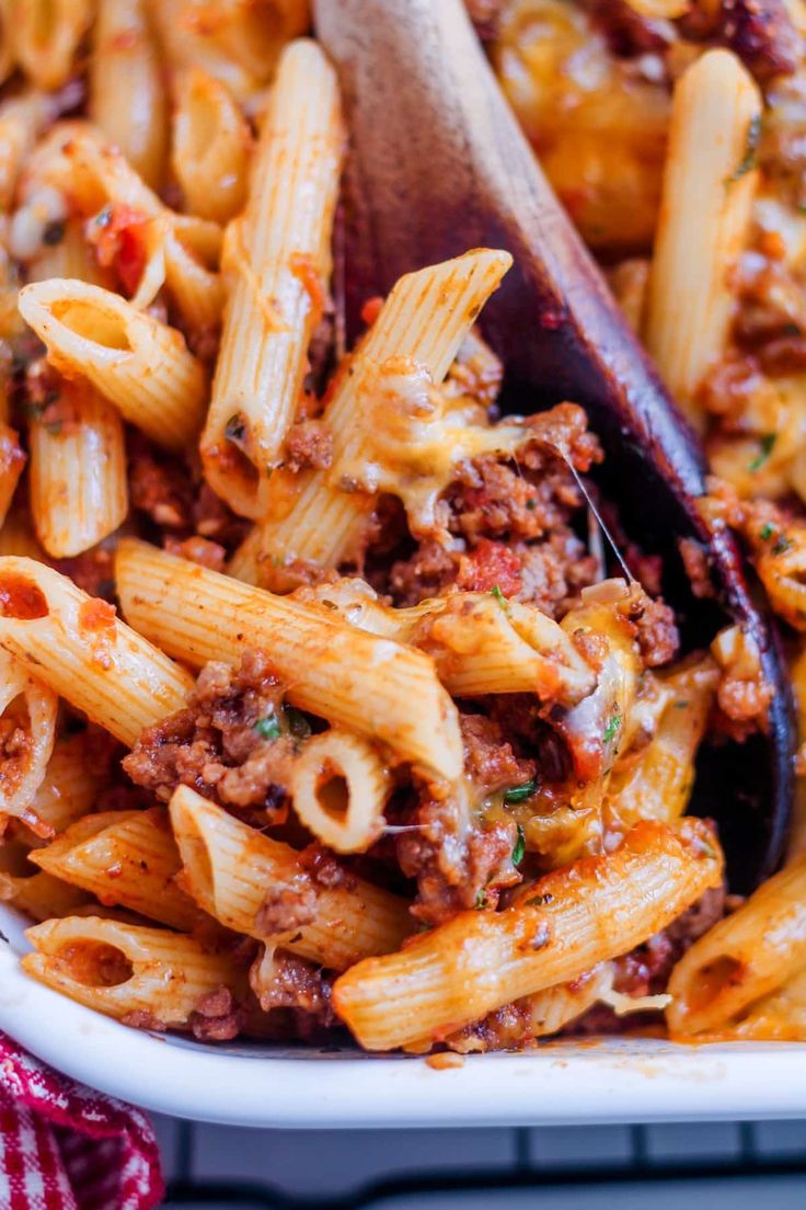 a pasta dish with meat and sauce in a white casserole dish on a red checkered cloth