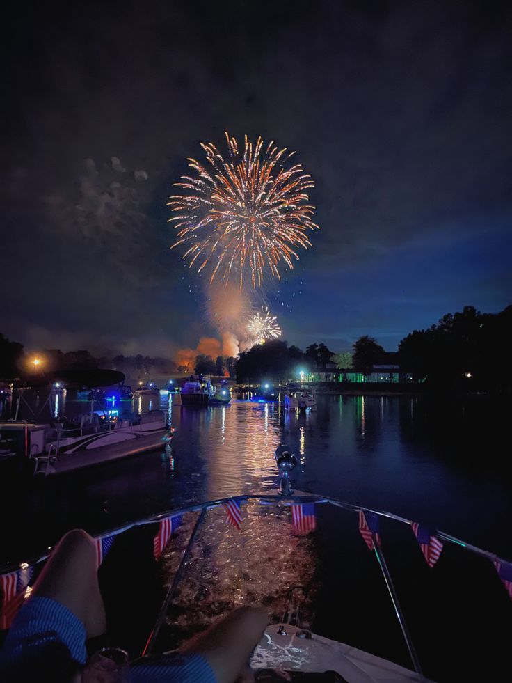 fireworks are lit up in the night sky over water with boats and people sitting at tables