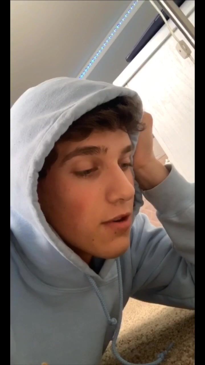 a young man wearing a hoodie is looking at his cell phone and holding his head with both hands