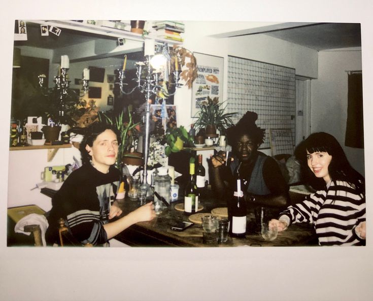 three people sitting at a table with wine bottles and glasses in front of the camera