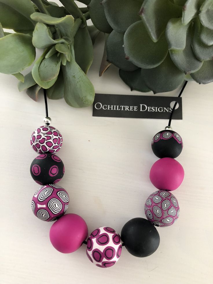 a pink and black beaded necklace on a table next to a succulent plant