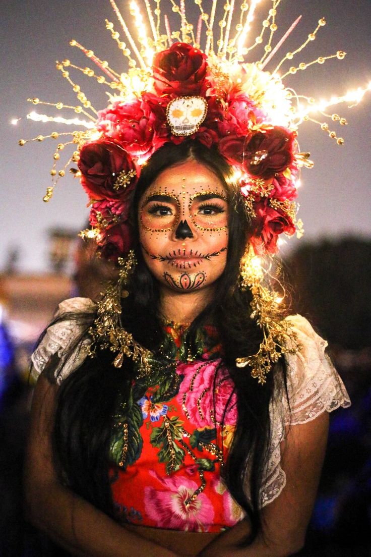 a woman with face paint and flowers on her head is posing for the camera at night