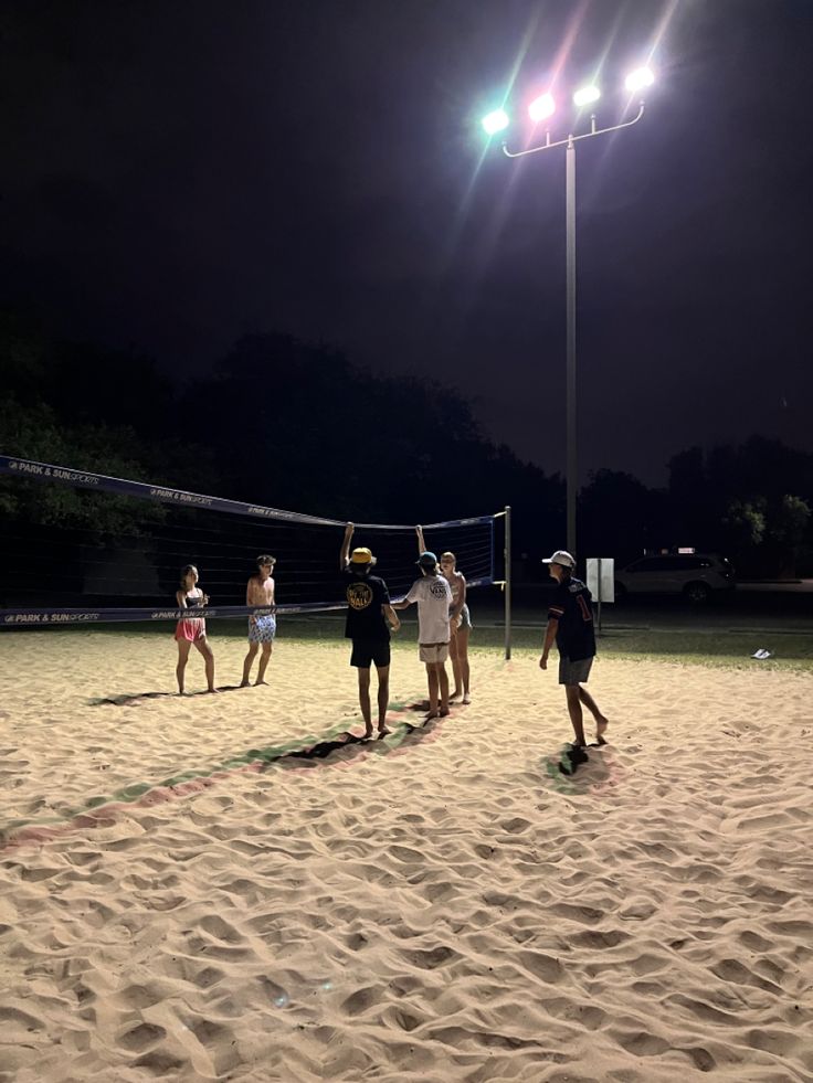 some people are playing volleyball in the sand at night with lights shining on the field