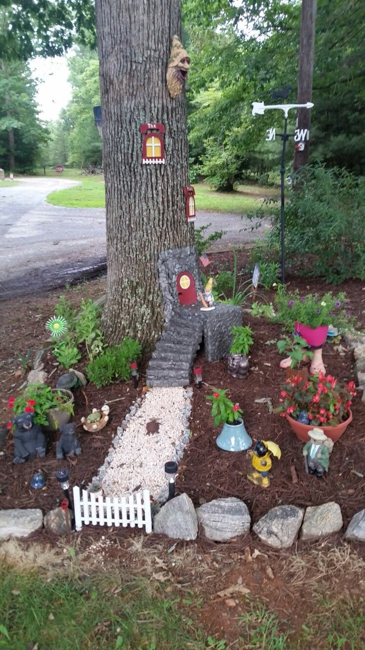 a small garden area with gnomes and plants in the ground next to a tree